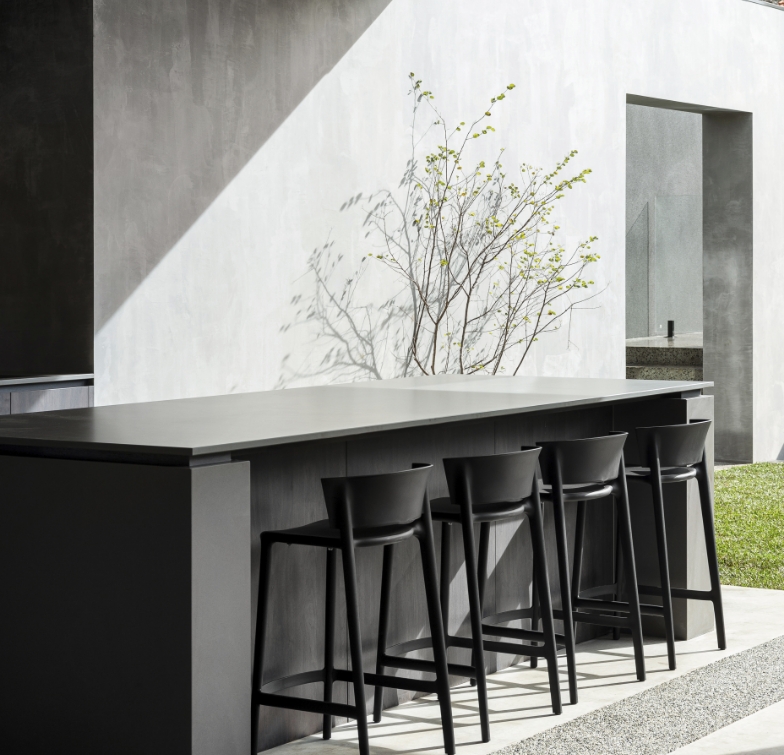 Modern outdoor kitchen with bar stools and concrete wall.